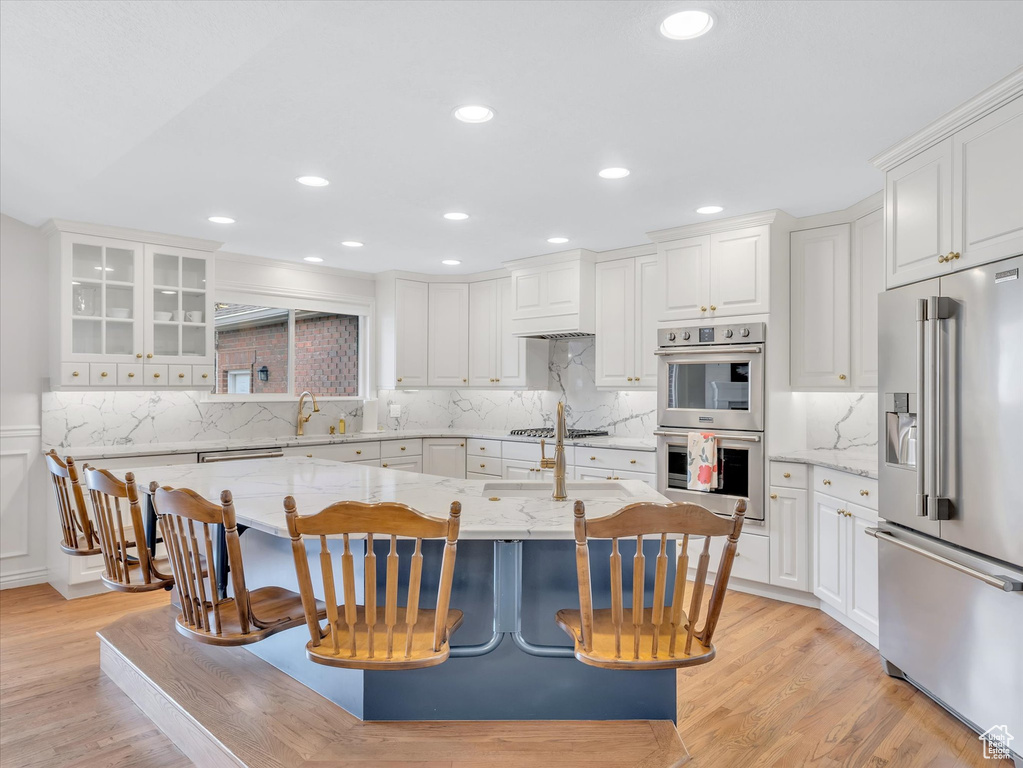 Kitchen featuring appliances with stainless steel finishes, white cabinetry, light stone counters, light wood-type flooring, and recessed lighting