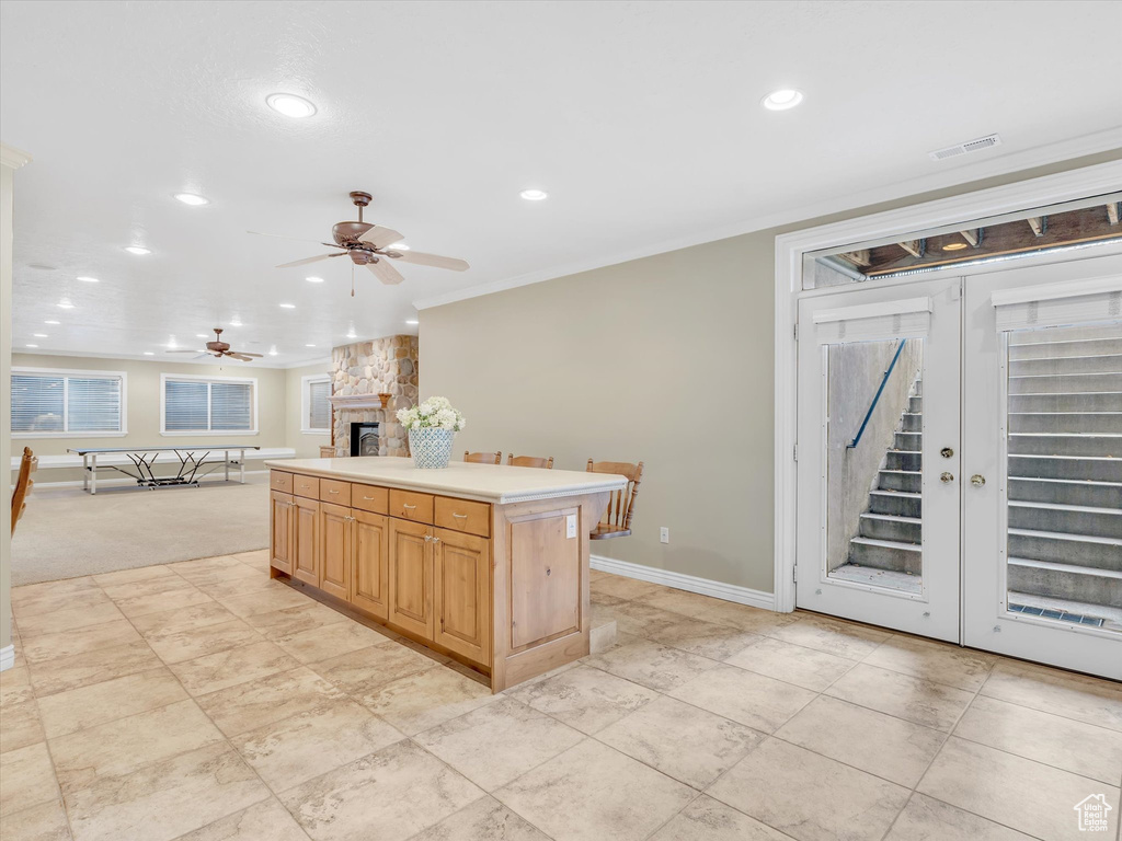 Kitchen featuring a stone fireplace, a ceiling fan, recessed lighting, a center island, and crown molding