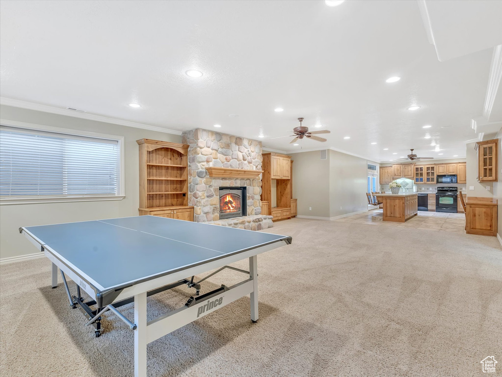 Recreation room with a ceiling fan, ornamental molding, recessed lighting, light colored carpet, and a fireplace