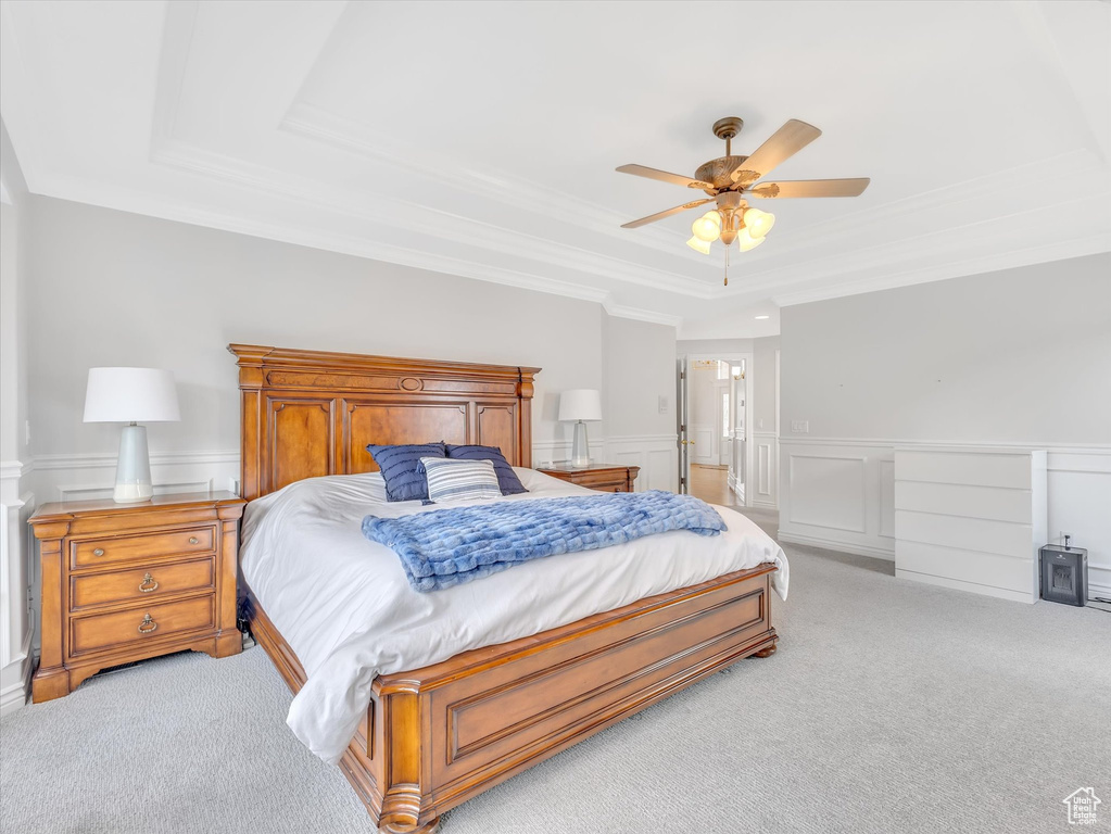 Bedroom featuring a raised ceiling, light carpet, ornamental molding, a decorative wall, and a wainscoted wall