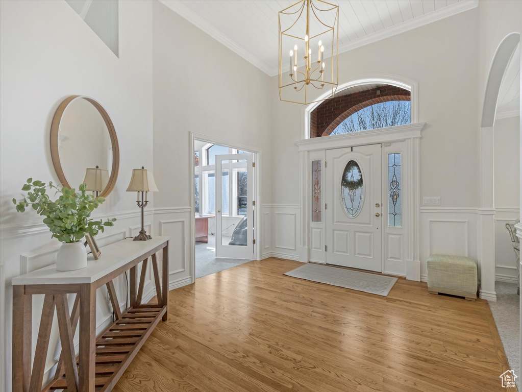 Entryway featuring high vaulted ceiling, a decorative wall, light wood-type flooring, a chandelier, and a wainscoted wall