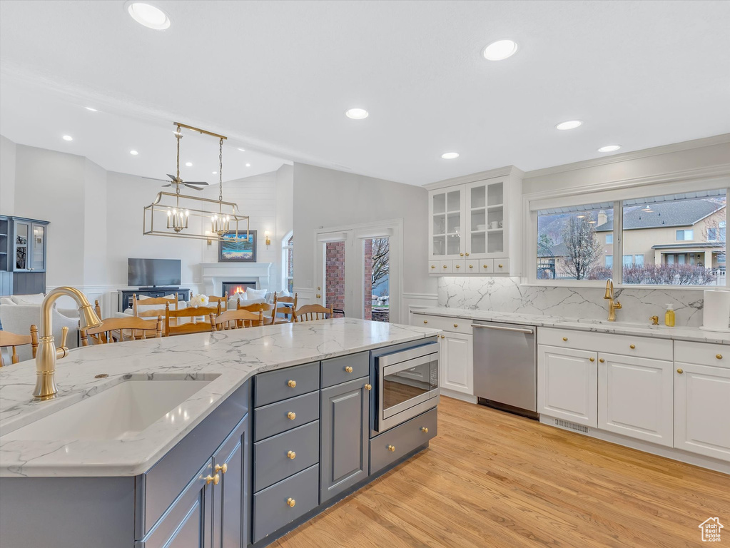 Kitchen with open floor plan, white cabinetry, stainless steel appliances, light wood-type flooring, and glass insert cabinets