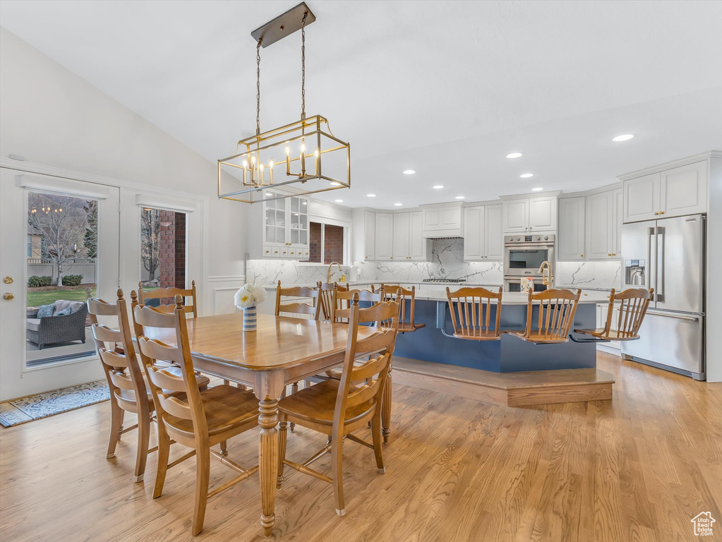 Dining area featuring light wood finished floors, a chandelier, recessed lighting, a decorative wall, and lofted ceiling