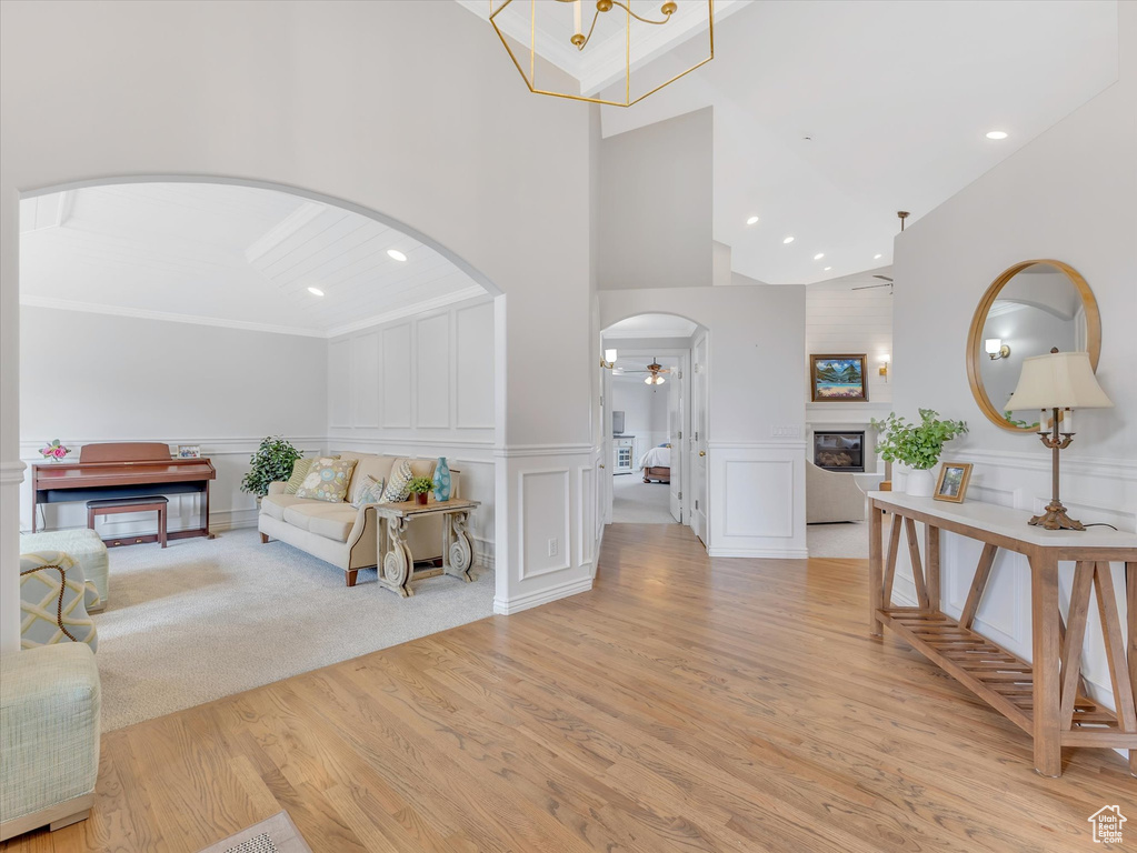 Living area with arched walkways, light wood finished floors, high vaulted ceiling, a decorative wall, and recessed lighting