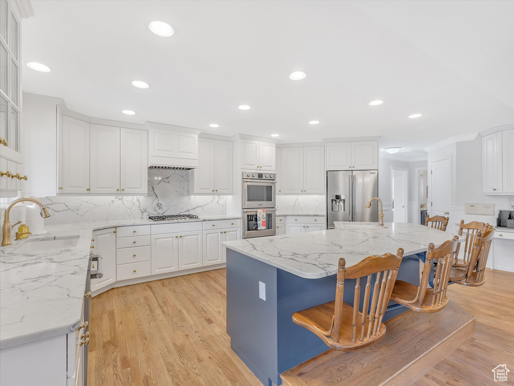 Kitchen featuring white cabinetry, a kitchen breakfast bar, appliances with stainless steel finishes, light wood-style flooring, and recessed lighting