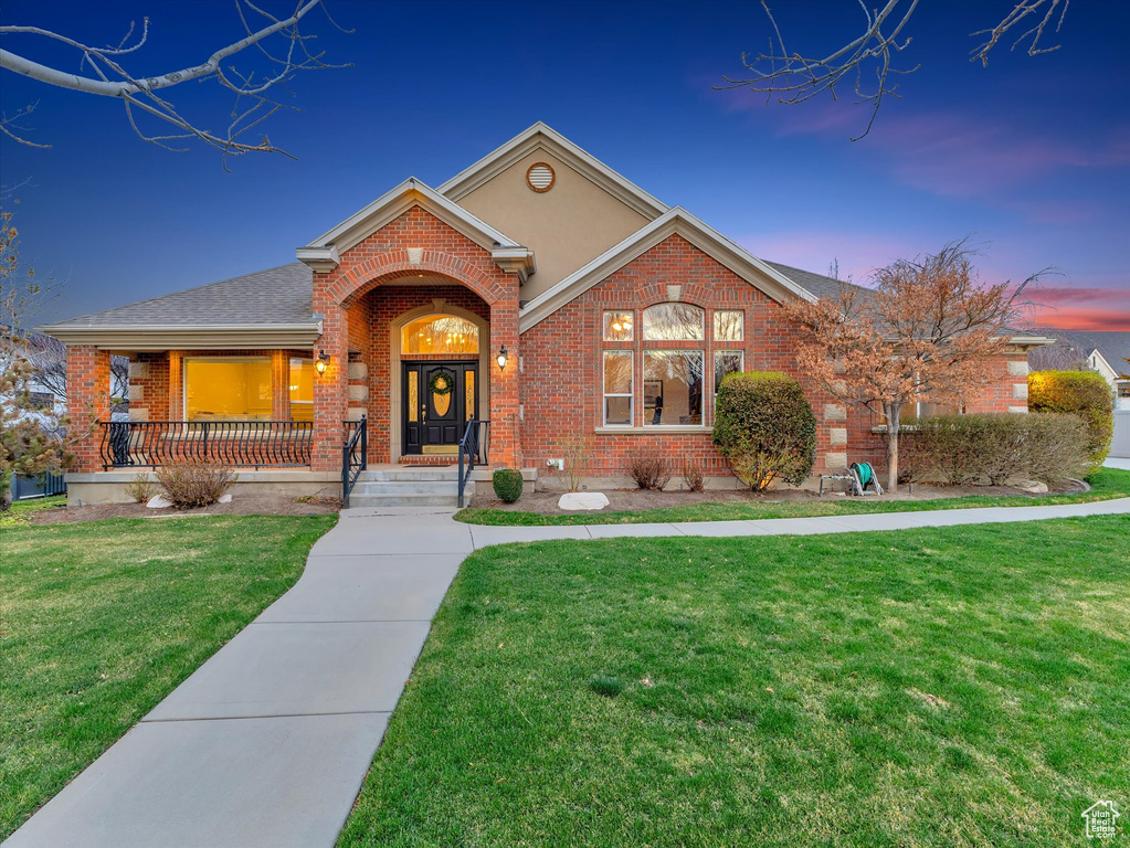 View of front of house featuring brick siding, a front yard, covered porch, and roof with shingles