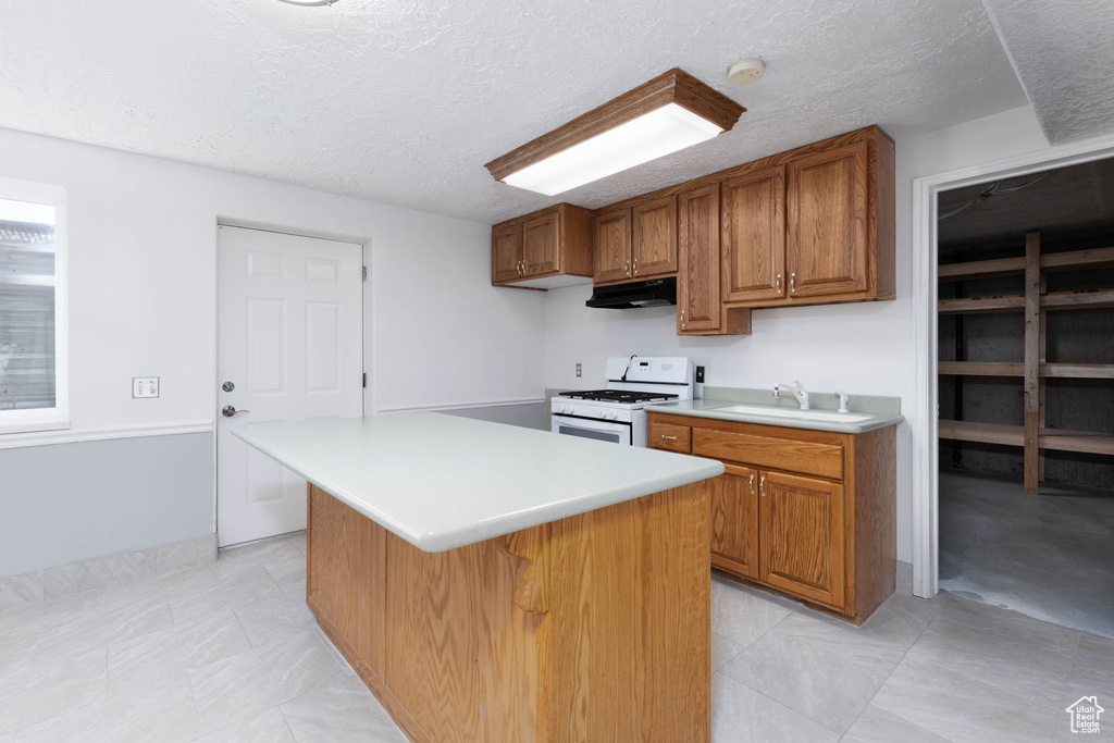 Kitchen featuring brown cabinetry, white range with gas stovetop, light countertops, a center island, and a textured ceiling