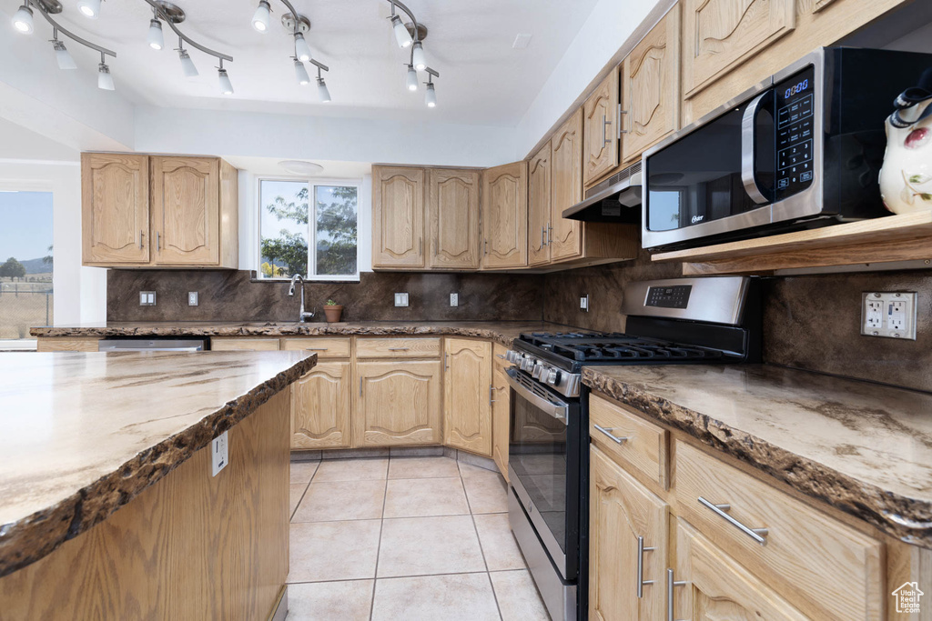 Kitchen with stainless steel appliances, decorative backsplash, light brown cabinetry, and light tile patterned flooring