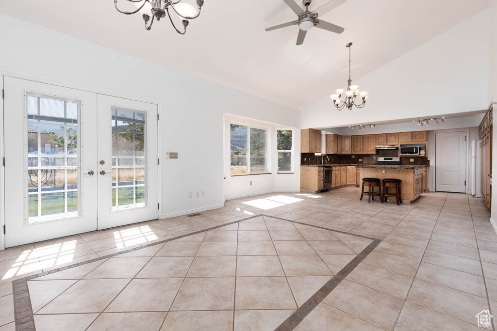 Unfurnished living room featuring a chandelier, light tile patterned floors, french doors, ceiling fan, and high vaulted ceiling