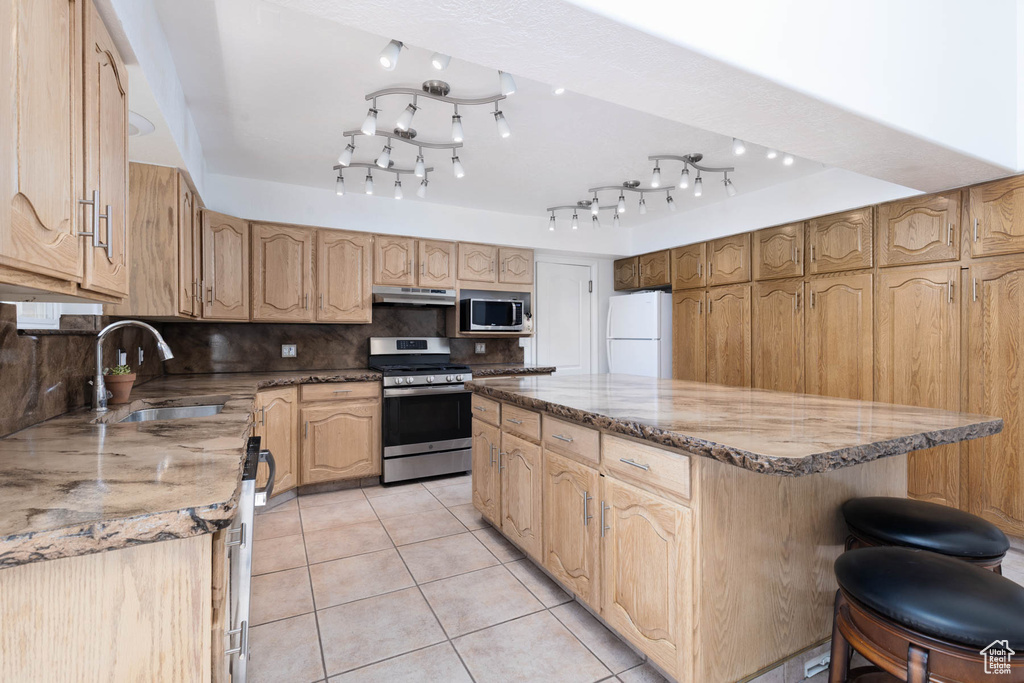 Kitchen featuring a center island, stainless steel appliances, light stone countertops, decorative backsplash, and light tile patterned flooring