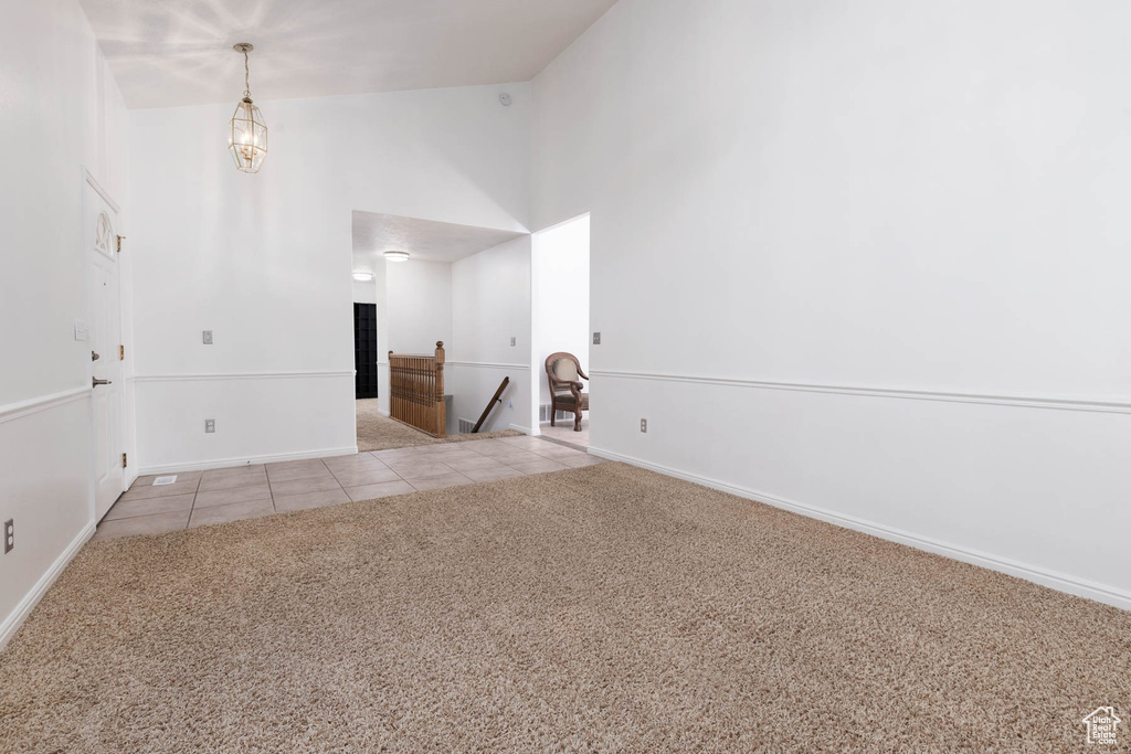 Empty room with high vaulted ceiling, light tile patterned flooring, and light colored carpet