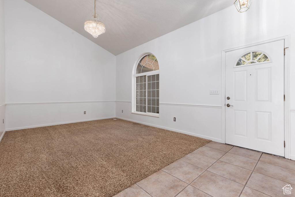 Foyer featuring high vaulted ceiling, light colored carpet, light tile patterned floors, and a chandelier