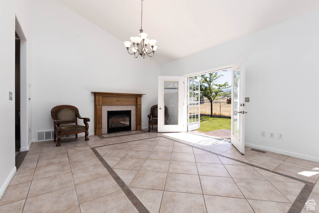 Unfurnished living room featuring light tile patterned floors, a chandelier, high vaulted ceiling, a tiled fireplace, and inlaid floor details