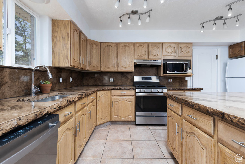 Kitchen with stainless steel appliances, dark stone countertops, decorative backsplash, and light tile patterned floors