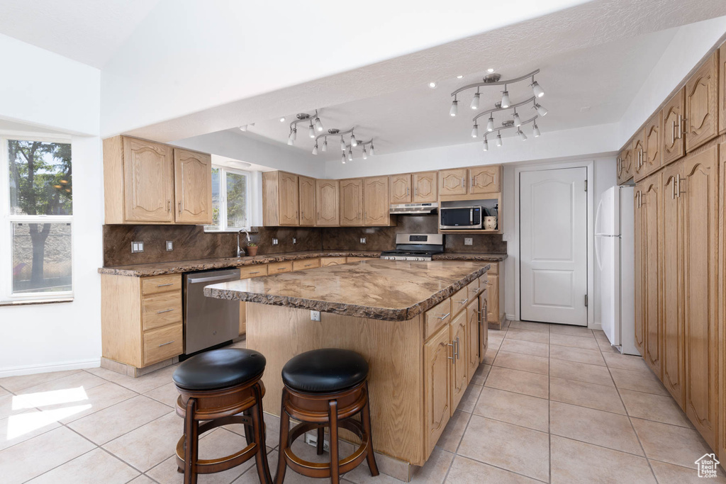 Kitchen with a kitchen island, light tile patterned floors, backsplash, appliances with stainless steel finishes, and a breakfast bar area