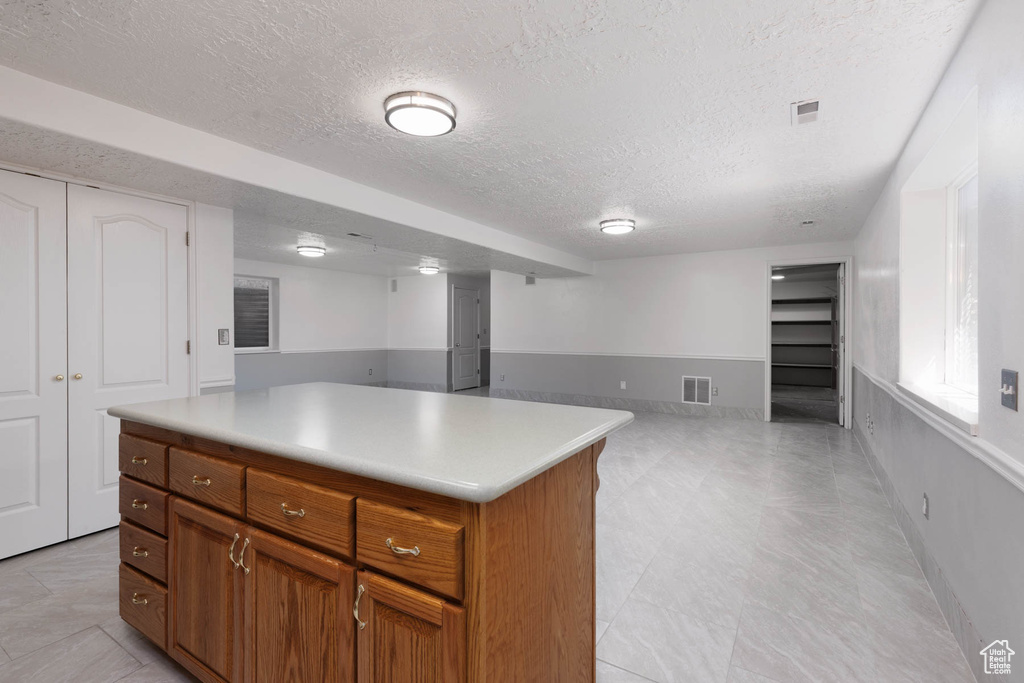 Kitchen with a textured ceiling, brown cabinets, open floor plan, light countertops, and a kitchen island