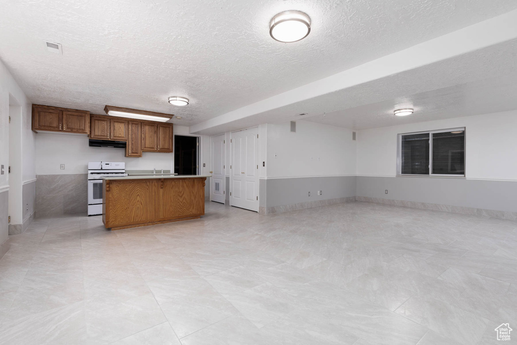 Kitchen with open floor plan, a textured ceiling, white gas range oven, brown cabinets, and a center island