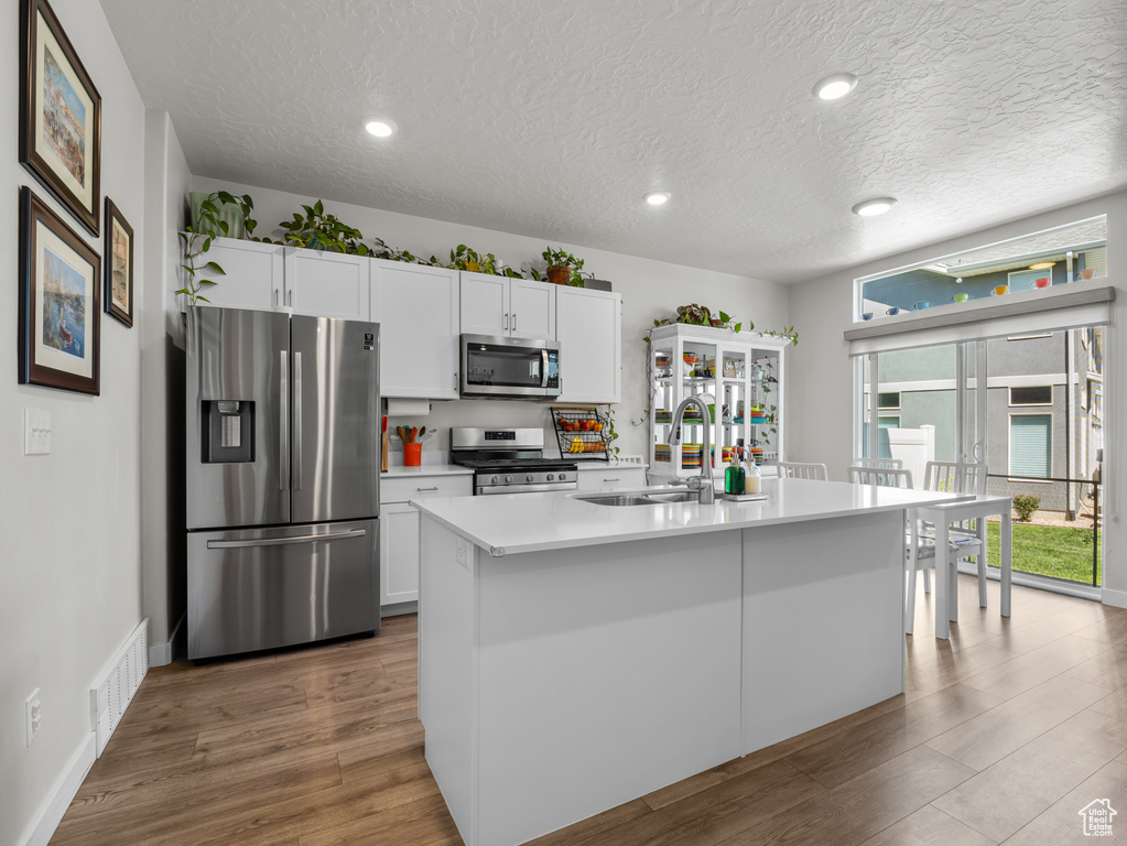 Kitchen with appliances with stainless steel finishes, wood finished floors, white cabinets, light countertops, and a textured ceiling