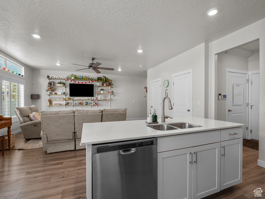Kitchen with dishwasher, a ceiling fan, wood finished floors, light countertops, and a center island with sink