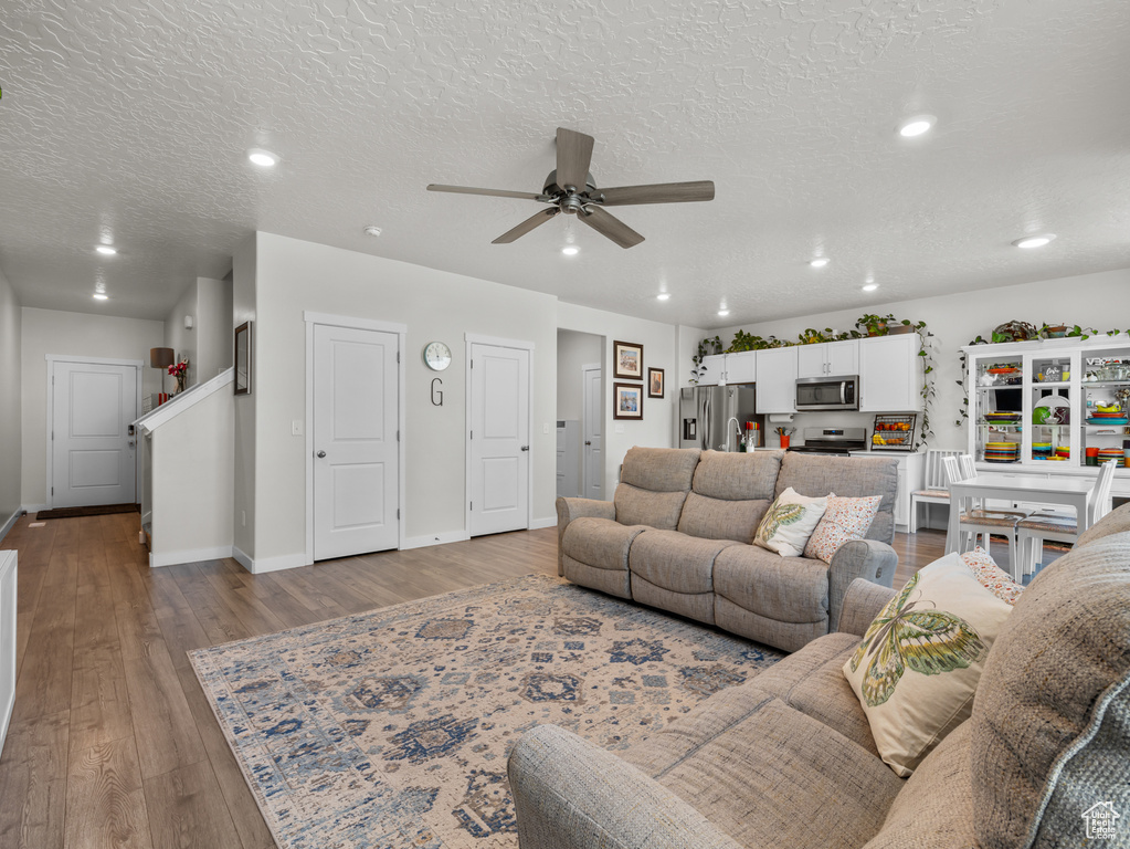 Living room with a ceiling fan, wood finished floors, recessed lighting, and a textured ceiling