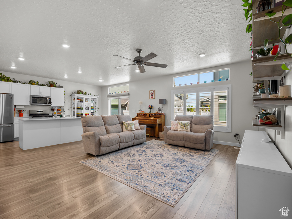 Living room featuring a ceiling fan, healthy amount of natural light, recessed lighting, light wood finished floors, and a textured ceiling