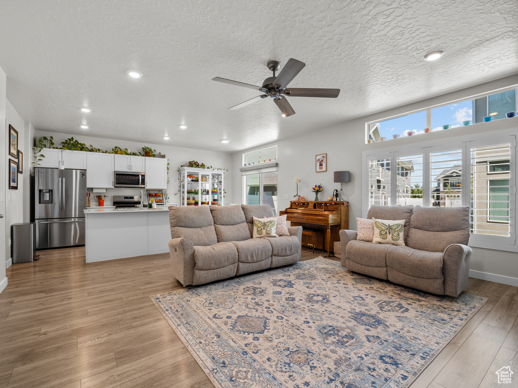 Living area featuring healthy amount of natural light, ceiling fan, light wood-style flooring, recessed lighting, and a textured ceiling