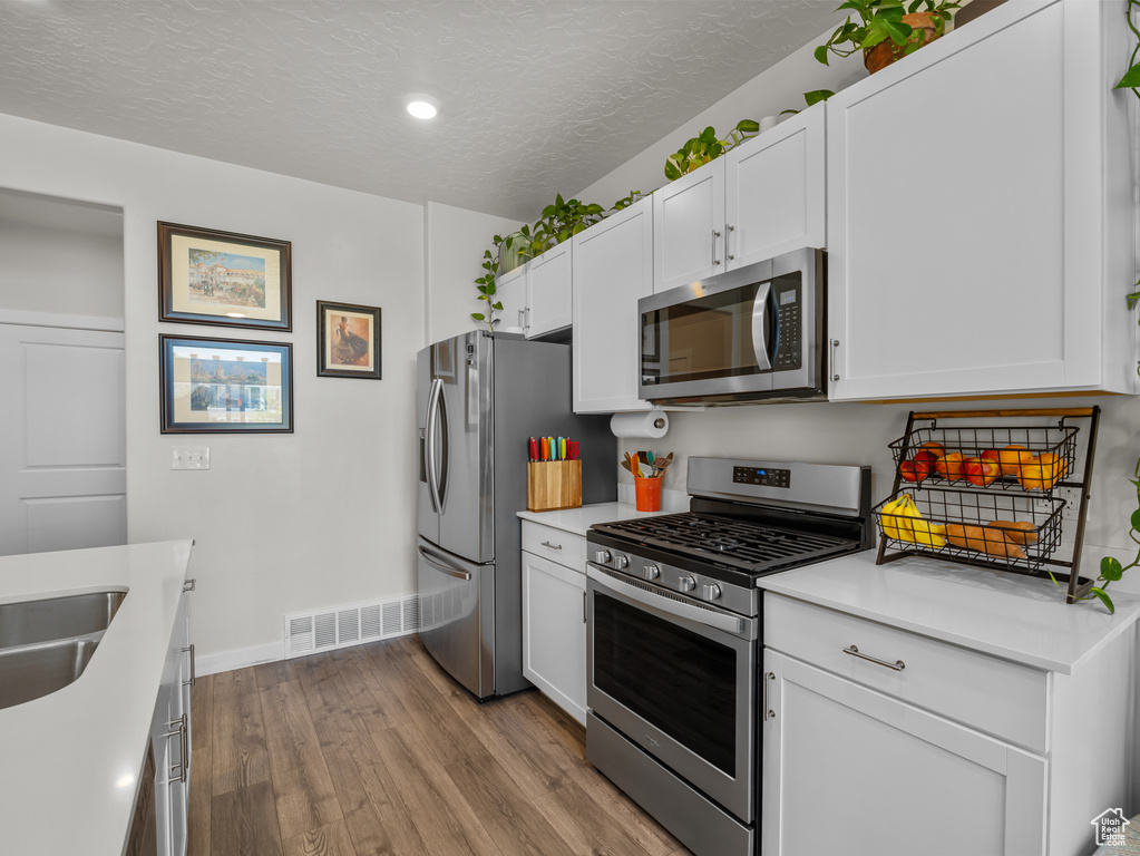 Kitchen featuring stainless steel appliances, wood finished floors, light countertops, white cabinetry, and a textured ceiling