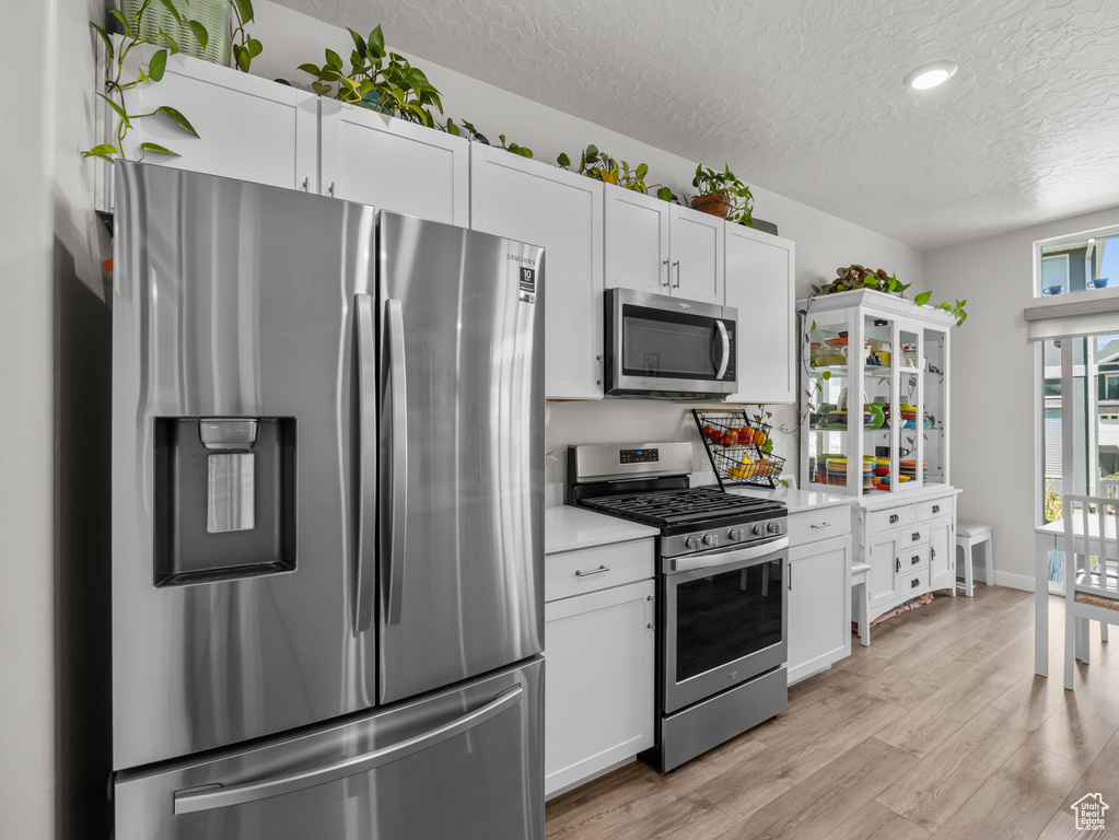 Kitchen with appliances with stainless steel finishes, a textured ceiling, light countertops, light wood finished floors, and white cabinets