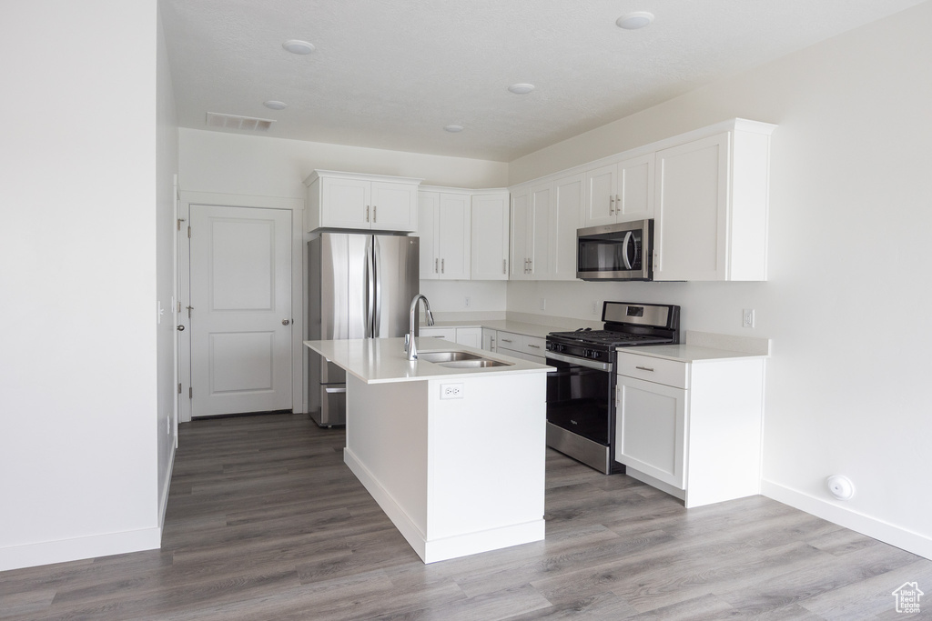 Kitchen with stainless steel appliances, white cabinets, wood finished floors, a kitchen island with sink, and light countertops