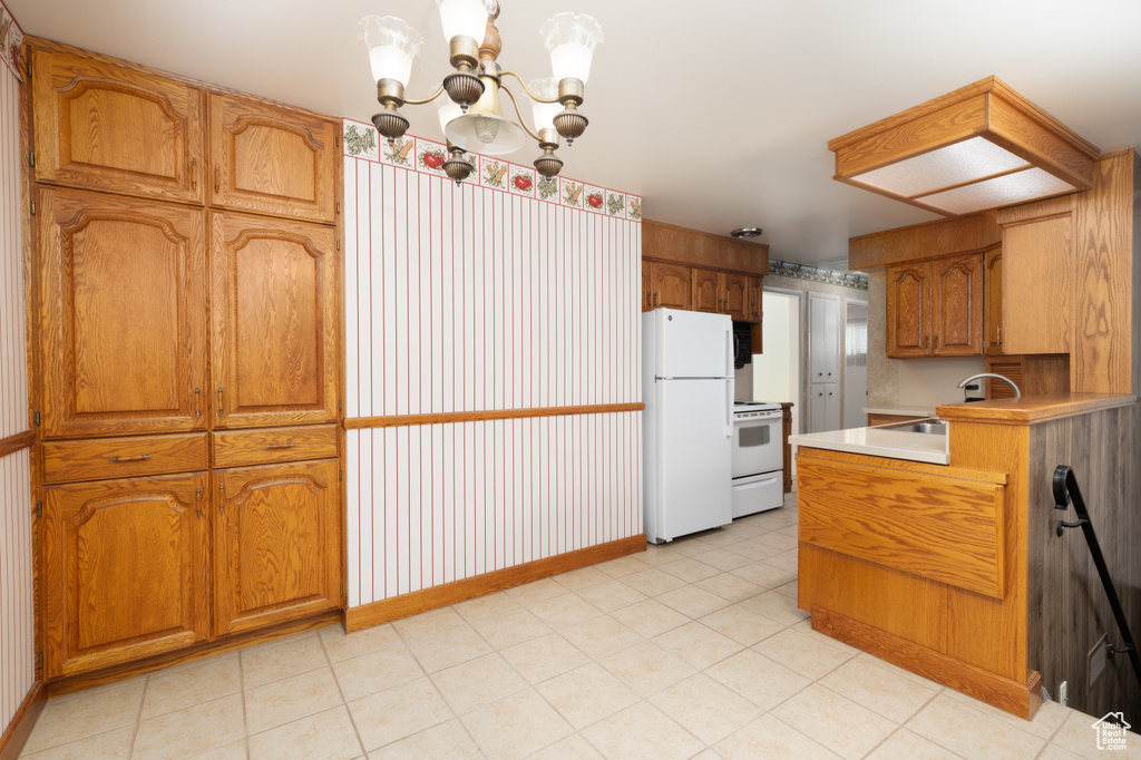 Kitchen featuring white appliances, brown cabinets, a chandelier, light countertops, and a peninsula