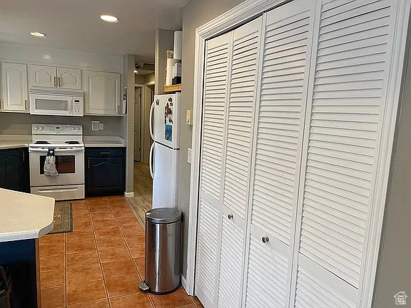 Kitchen featuring white appliances, light countertops, tile patterned floors, white cabinetry, and recessed lighting
