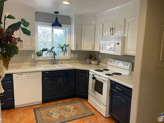 Kitchen with white appliances, white cabinets, light countertops, light tile patterned floors, and hanging light fixtures