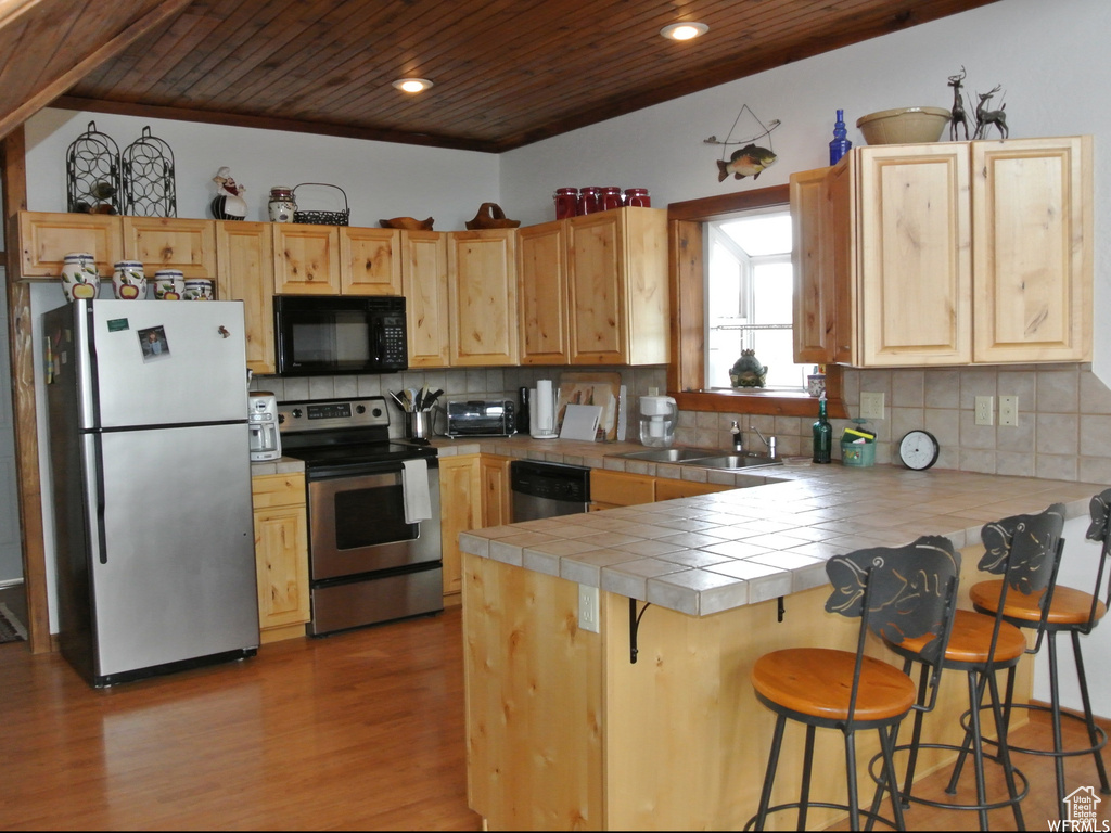 Kitchen featuring wood ceiling, stainless steel appliances, tile countertops, wood finished floors, and a peninsula