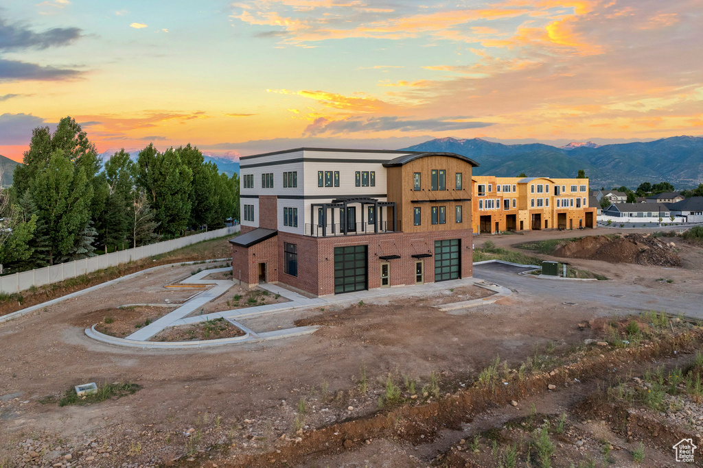 Back of property at dusk with an attached garage, a mountain view, and dirt driveway