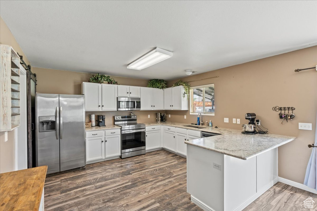 Kitchen featuring appliances with stainless steel finishes, a peninsula, dark wood-type flooring, and white cabinetry