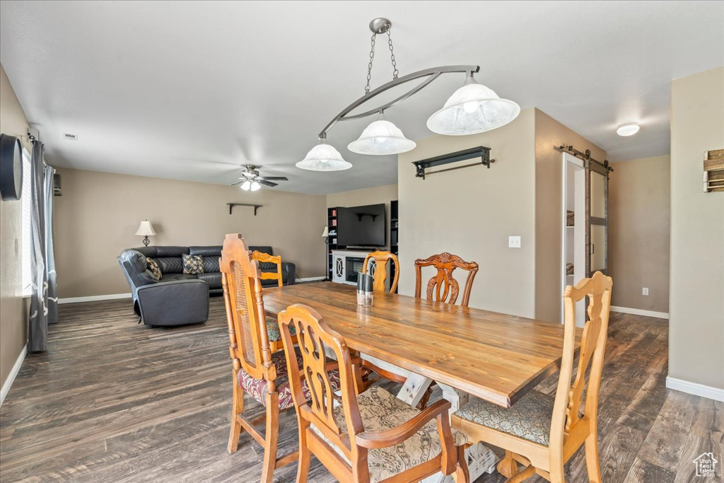 Dining room with a barn door, dark wood-style floors, and ceiling fan