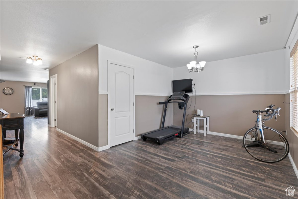 Exercise room with dark wood-type flooring and a chandelier