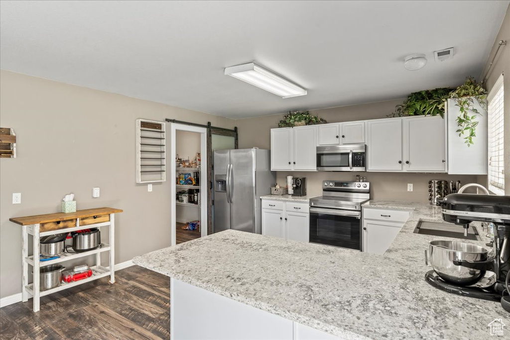 Kitchen with appliances with stainless steel finishes, a peninsula, dark wood-style flooring, light stone countertops, and white cabinets