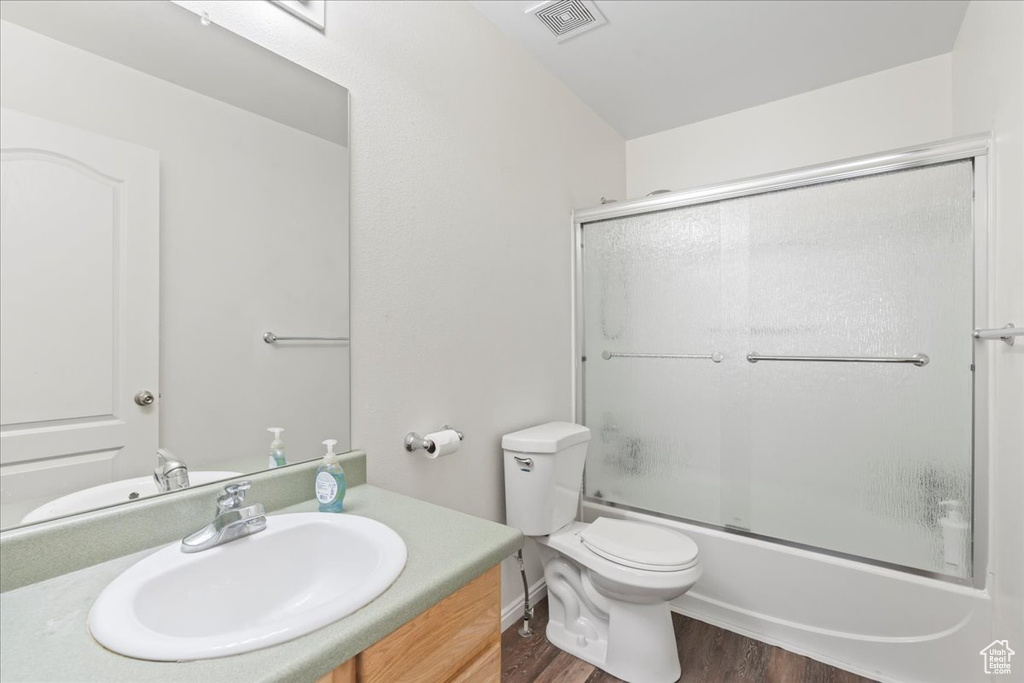 Bathroom with wood finished floors, vanity, and combined bath / shower with glass door