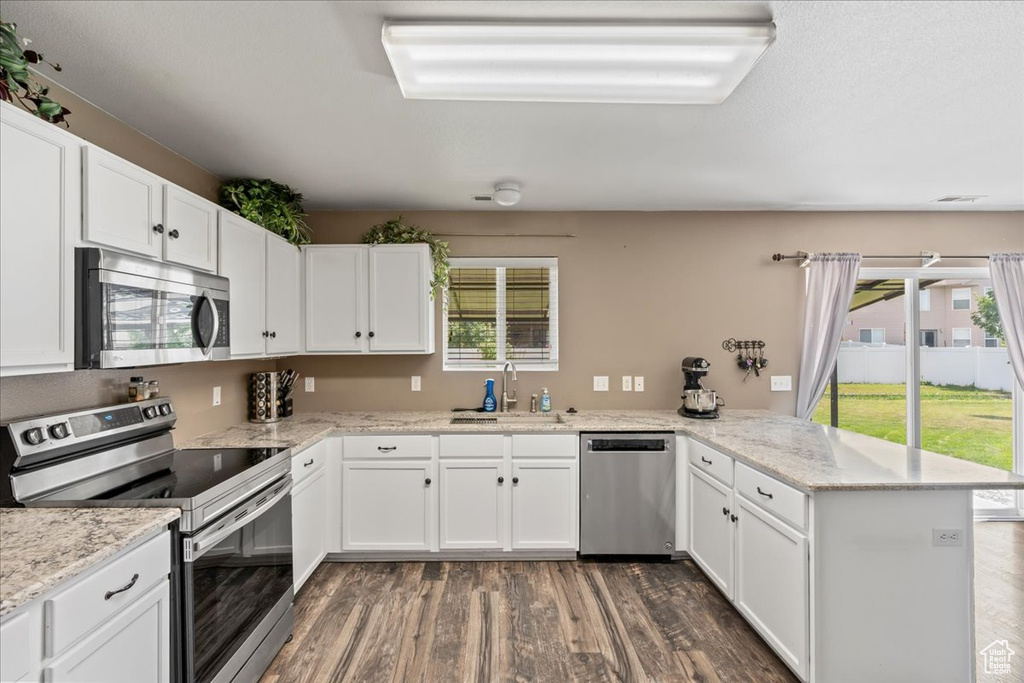 Kitchen featuring stainless steel appliances, a peninsula, dark wood finished floors, white cabinetry, and light stone counters