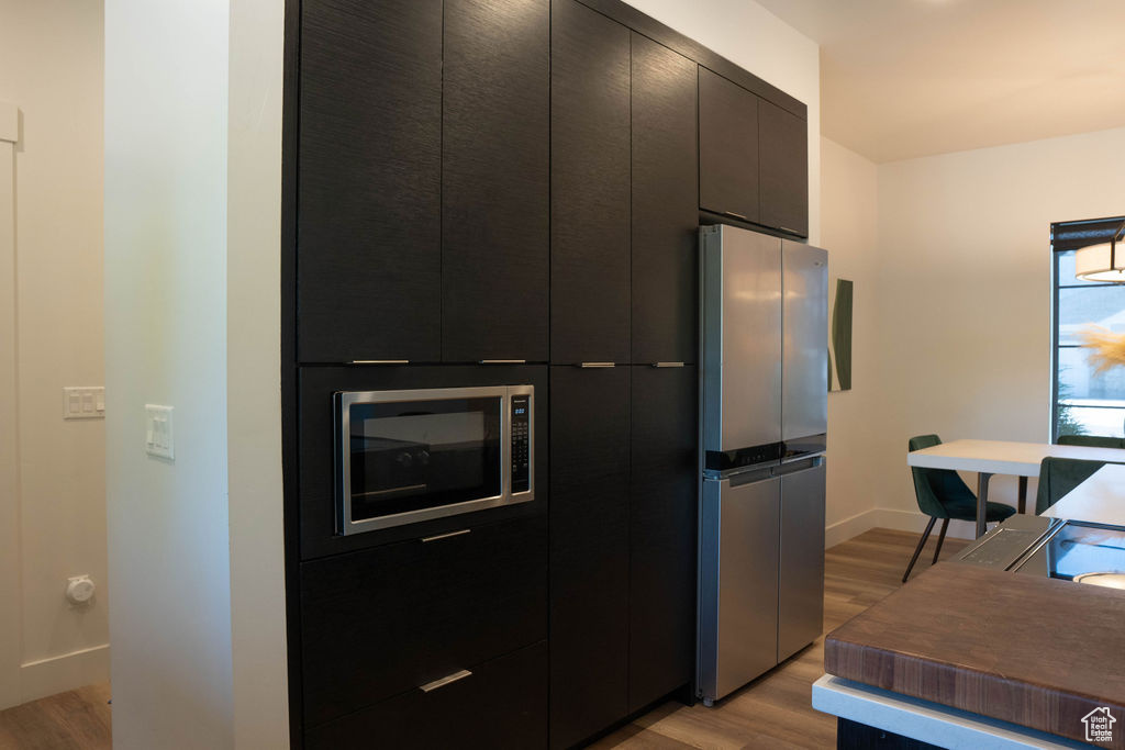 Kitchen with appliances with stainless steel finishes, light wood-style floors, modern cabinets, and dark cabinetry