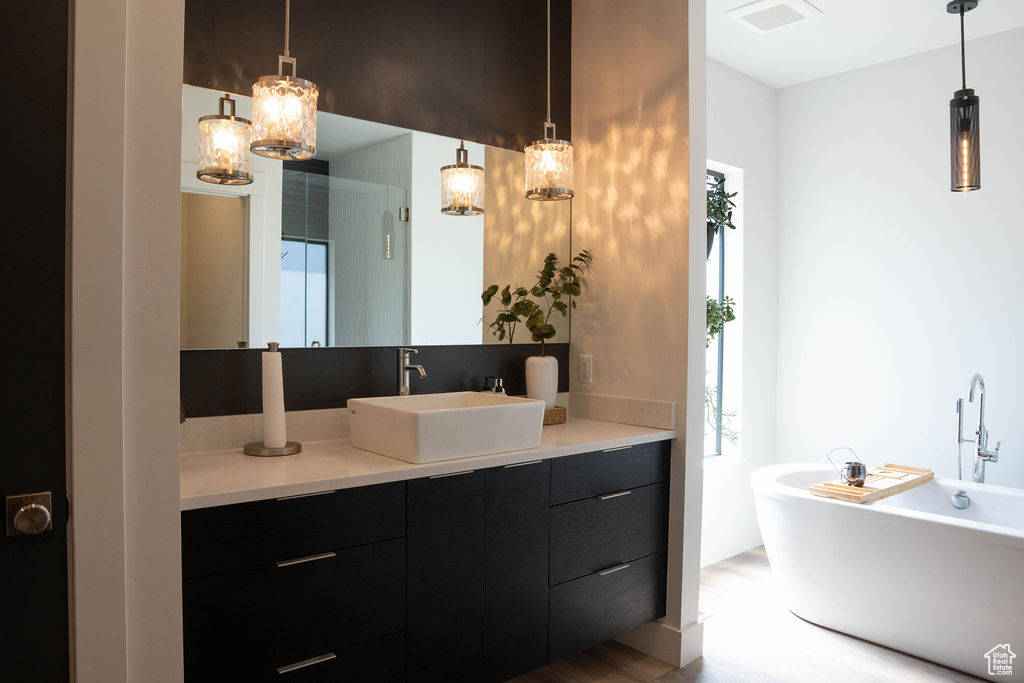 Full bath with vanity, a soaking tub, a chandelier, and wood finished floors