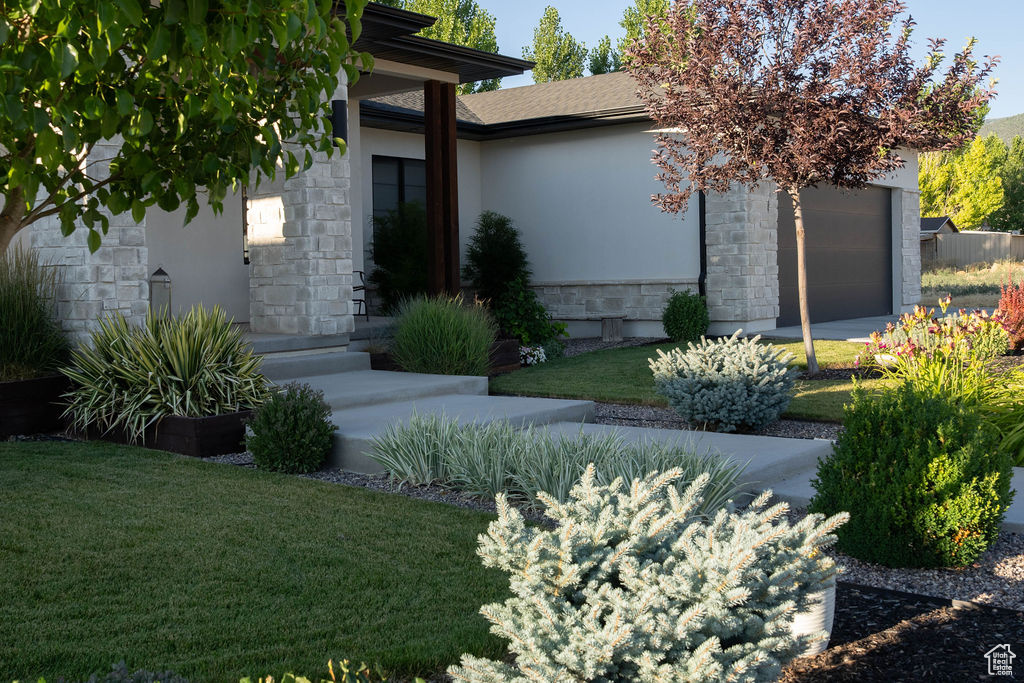 Entrance to property with stone siding, an attached garage, stucco siding, and a yard