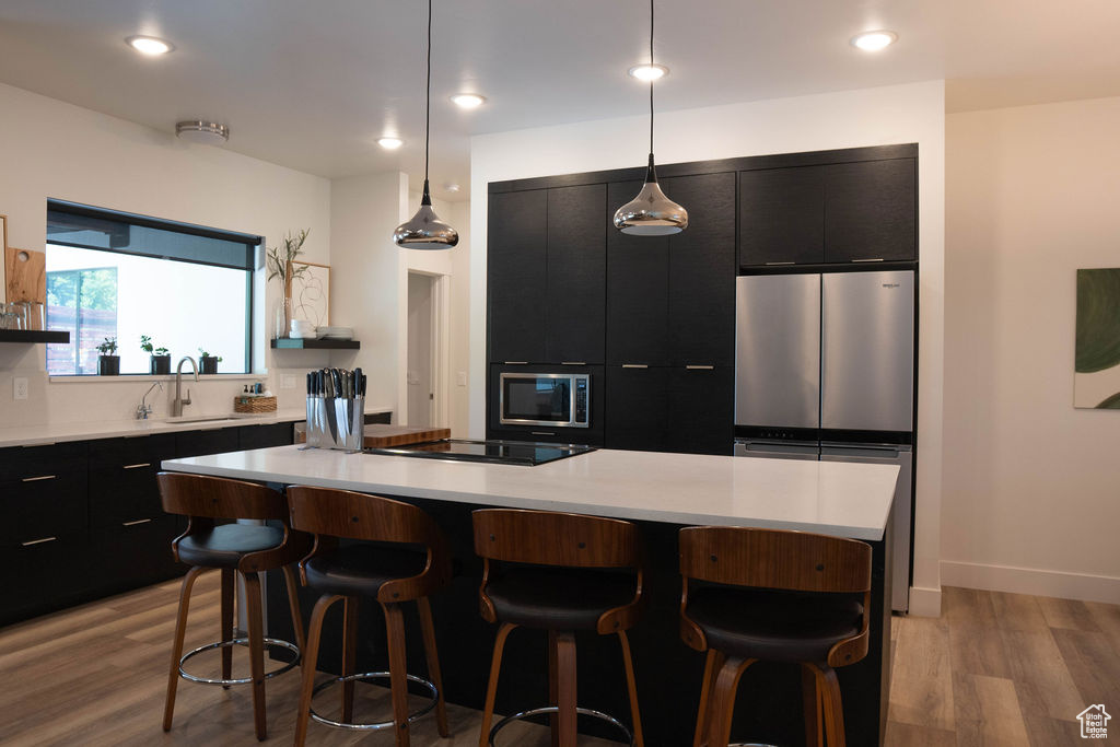 Kitchen with dark cabinets, light wood-type flooring, a kitchen breakfast bar, light countertops, and a center island