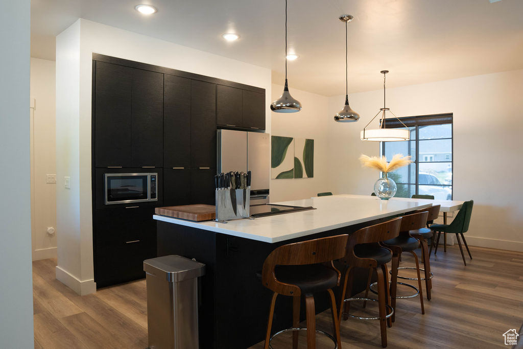 Kitchen featuring dark cabinets, wood finished floors, a center island, light countertops, and a breakfast bar