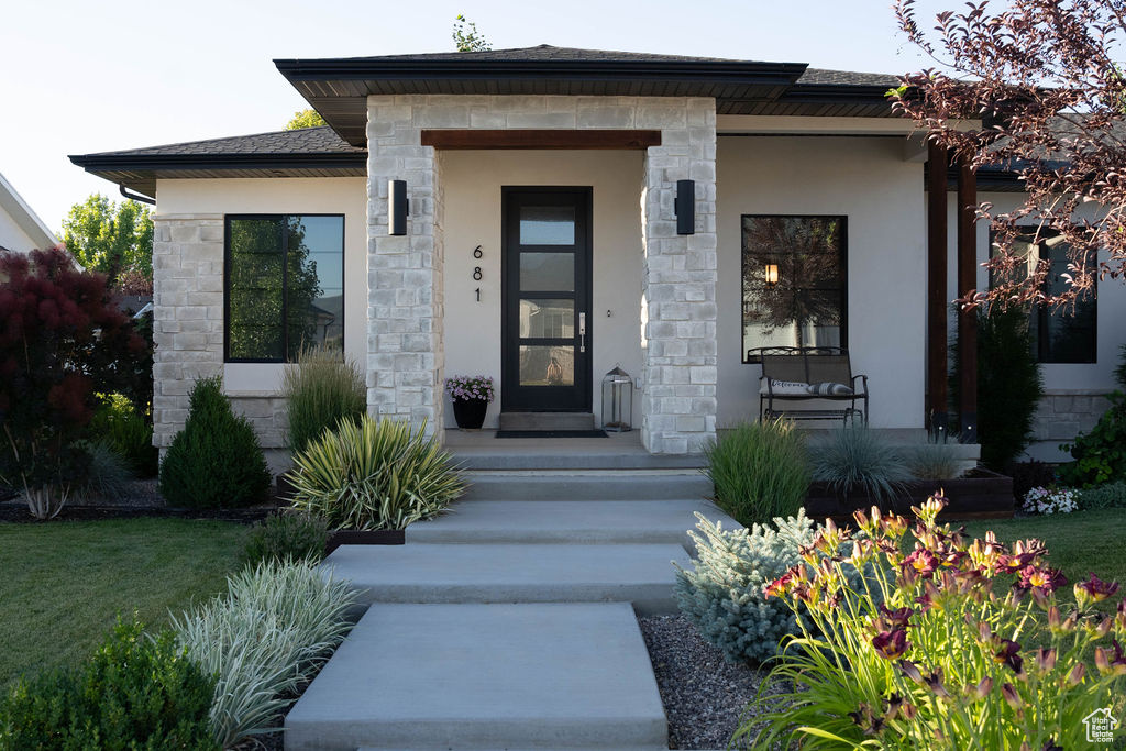 View of exterior entry featuring stone siding, covered porch, and stucco siding