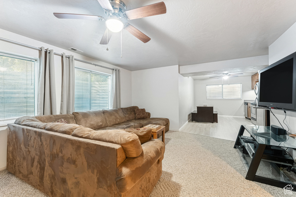 Living area with ceiling fan, light carpet, and healthy amount of natural light