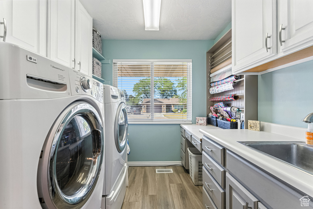 Laundry room featuring cabinet space, separate washer and dryer, and light wood-style flooring