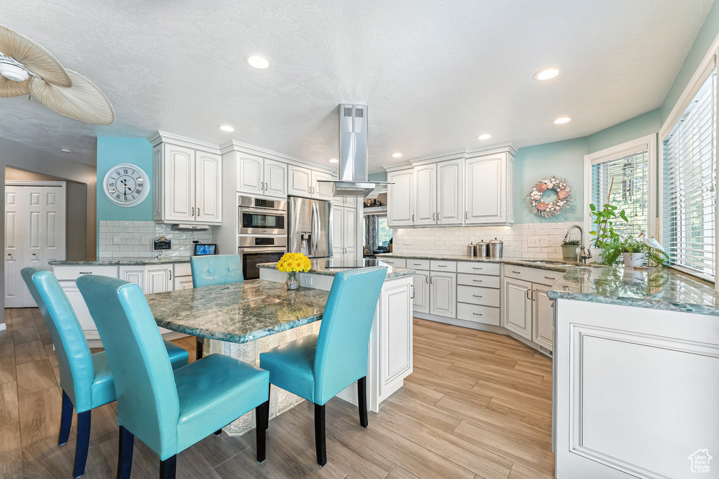 Kitchen with backsplash, stainless steel appliances, island range hood, dark stone counters, and white cabinetry
