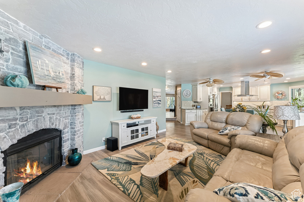 Living room featuring a ceiling fan, a stone fireplace, recessed lighting, and light wood-type flooring